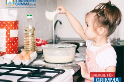 Ein kleines Mädchen steht vor einem Gasherd und rührt Pfannkuchenteig an.
