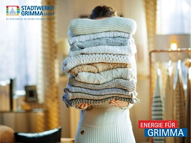EIne Frau steht in einem hellen Raum und hält einen Stapel kuscheliger wollener Pullover hoch. © Stadtwerke Grimma GmbH
