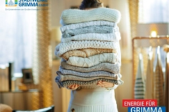 EIne Frau steht in einem hellen Raum und hält einen Stapel kuscheliger wollener Pullover hoch.