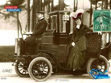 Eine schwarzweiße Postkarte aus dem Jahr 1901, abgebildet ist eine französische Schauspielerin vor einem historischen Elektro-Auto, vorne sitzt der Fahrer, ähnlich wie bei einer Kutsche